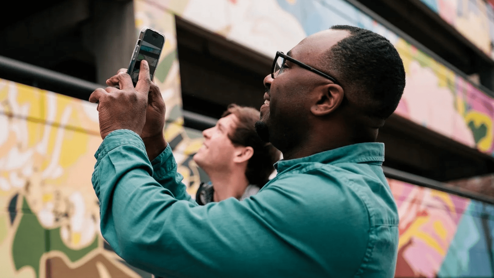 Two men taking a picture of a mural on a parking garage. 