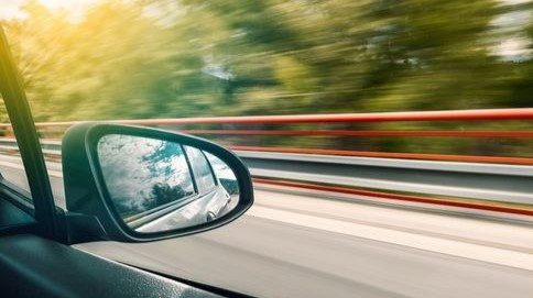 A car's side mirror. The landscape outside the car is blurred to indicate fast movement. 