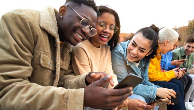 A group of smiling young people looking at a smartphone. 